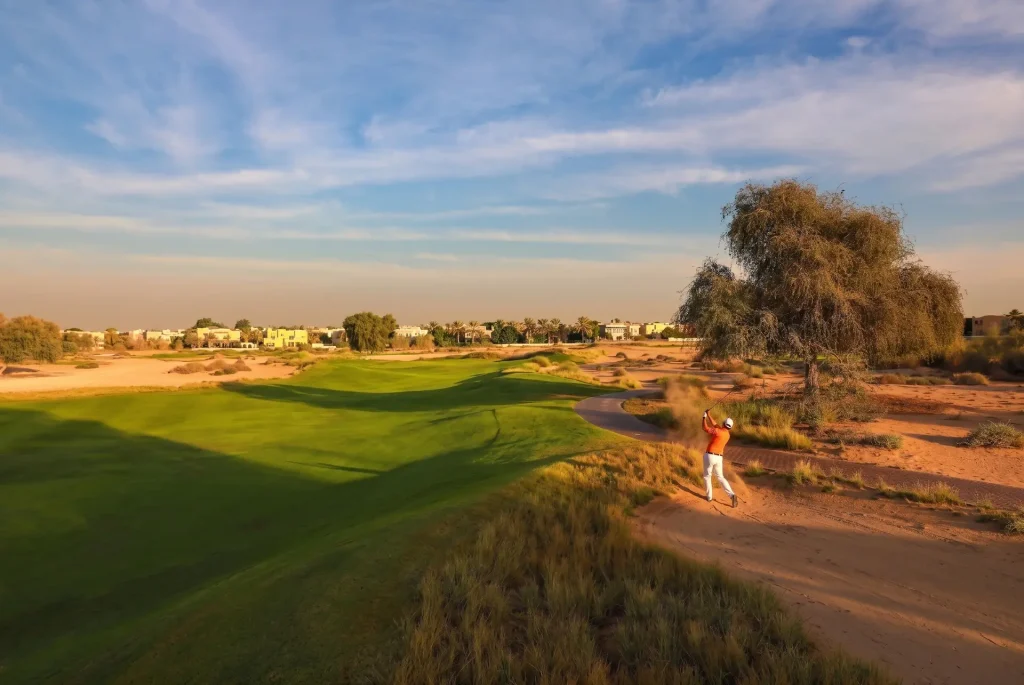 Golfer teeing off on the desert-themed championship golf course at Arabian Ranches Dubai, showcasing luxury community living for potential home buyers